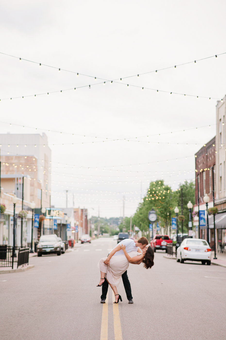 engaged couple kissing in the middle of the street with string lights