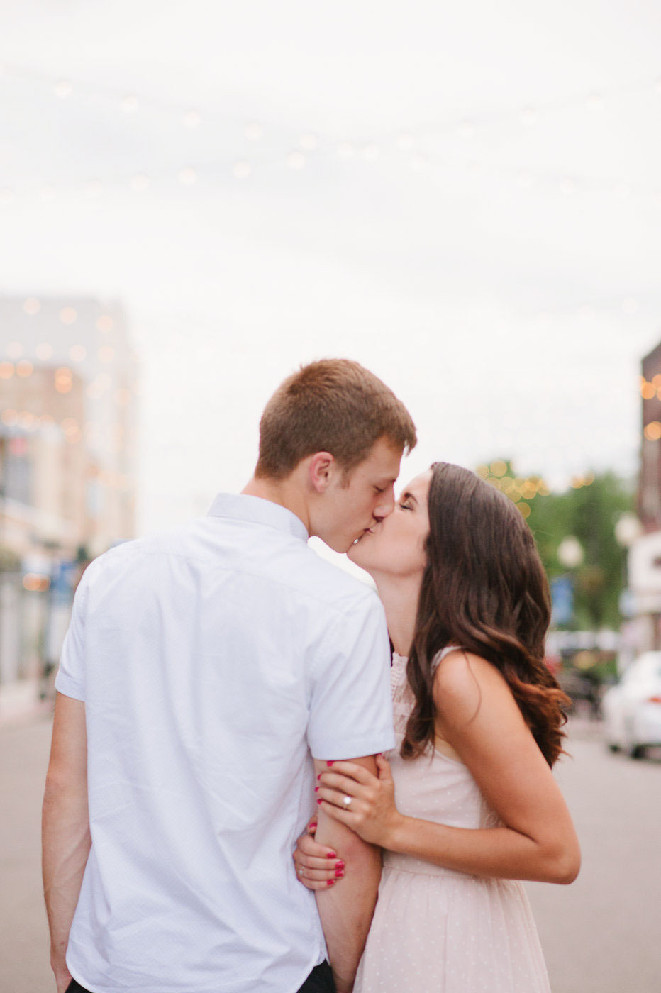engaged couple kissing in the middle of the street with string lights