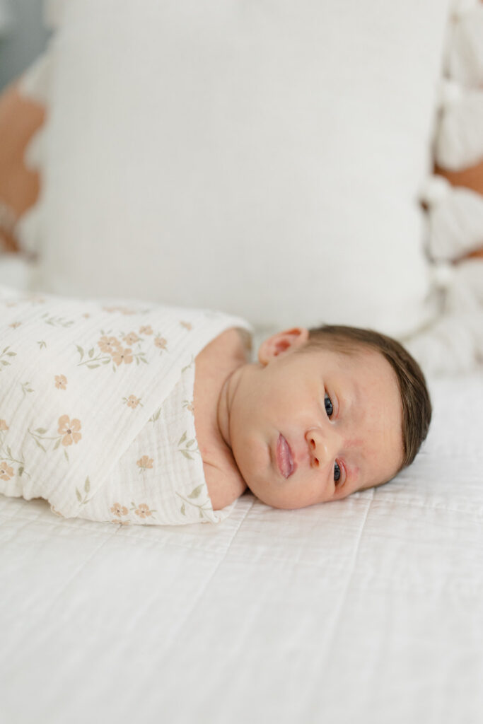 baby in a floral swaddle laying on a plush white bed for an in home newborn session with cleveland family photographer