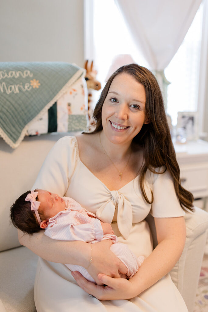 Mother cradles her newborn in a softly decorated nursery, wearing a neutral dress that offers timeless what to wear inspiration for in-home newborn photos by a Cleveland family photographer.