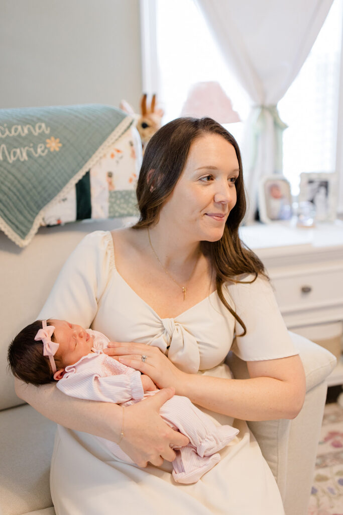 Mother cradles her sleeping newborn in a cozy nursery, wearing a soft neutral dress that provides timeless what to wear inspiration for in-home newborn photos by a Cleveland family photographer.