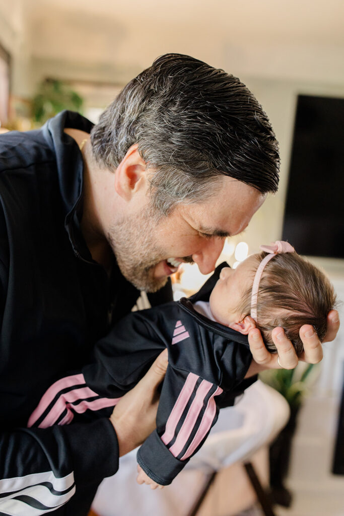 Father smiles nose-to-nose with his newborn dressed in a coordinating tracksuit, capturing a playful moment in heartfelt newborn photos with unique what to wear inspiration.
