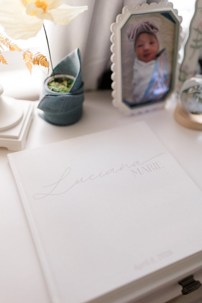 Personalized newborn keepsake album displayed beside a framed baby photo in the nursery, highlighting meaningful details often documented during newborn photos.