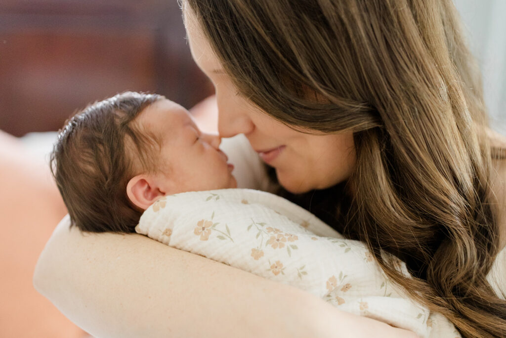 Mother gently cradles her sleeping newborn wrapped in a neutral floral swaddle, highlighting intimate newborn photos with timeless what to wear inspiration from a Cleveland family photographer.