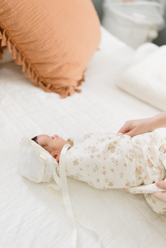 Swaddled newborn wearing a delicate bonnet and floral wrap on a bed, capturing a timeless styling detail for elegant newborn photos by a Cleveland family photographer.