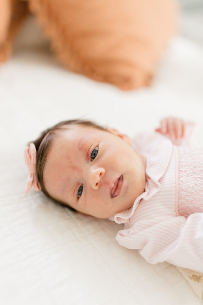 Close-up portrait of a newborn in a pink smocked outfit and bow headband, showcasing a classic what to wear choice for natural newborn photos.