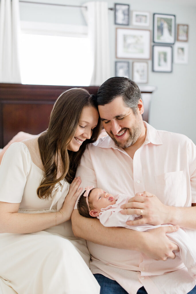 Parents in coordinated neutral outfits smile at their newborn during an in-home session, featuring classic what to wear inspiration for heartfelt newborn photos.