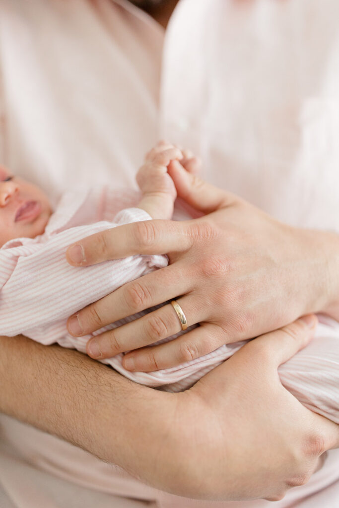 lose-up of a father gently holding his newborn's tiny hands during intimate in-home newborn photos, capturing a meaningful family detail.