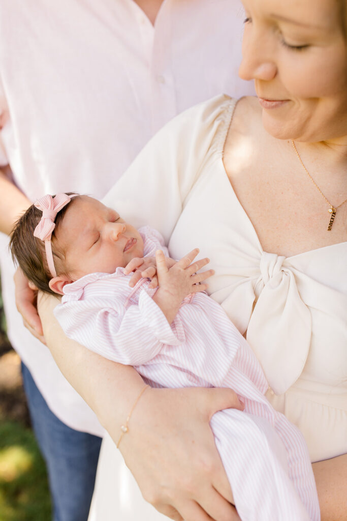 Mother cradles her sleeping newborn outdoors, highlighting the baby's delicate features and pink outfit in soft natural light.