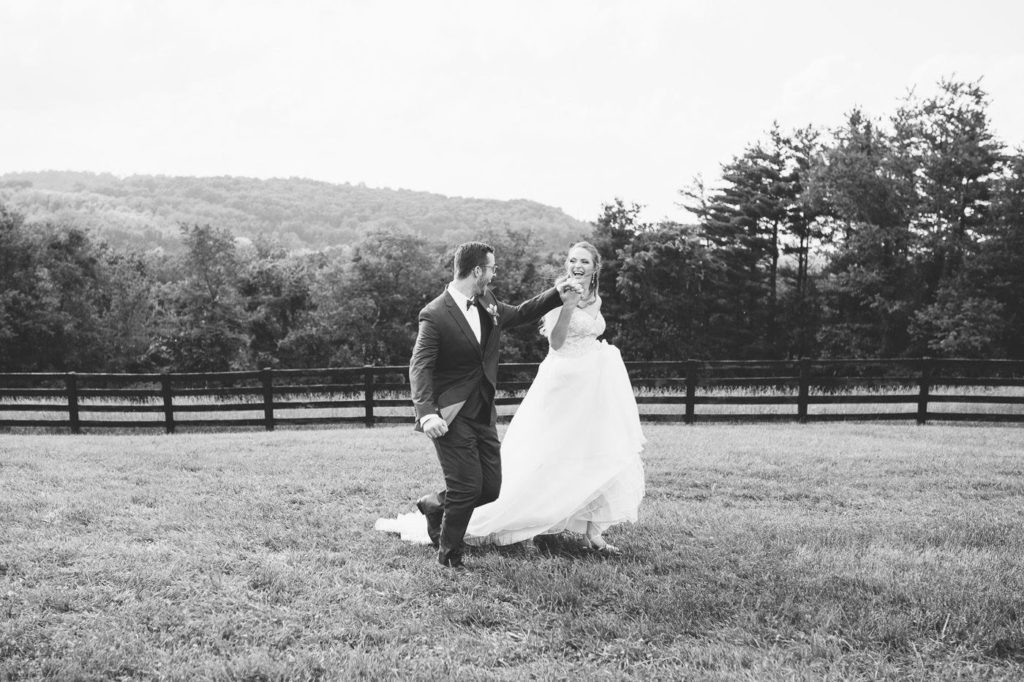 black and white image of bride and groom running in an open field