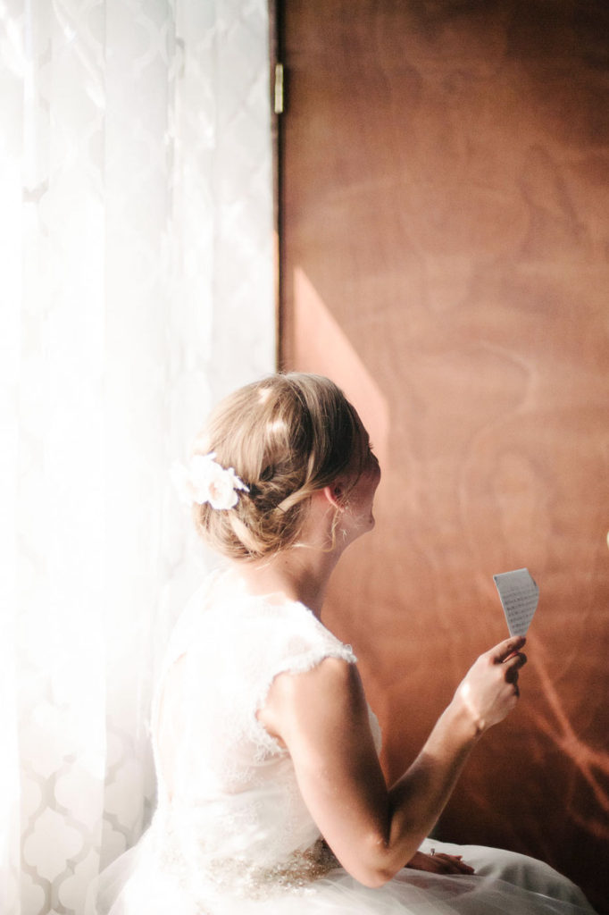 bride sitting by a window reading a note from her groom