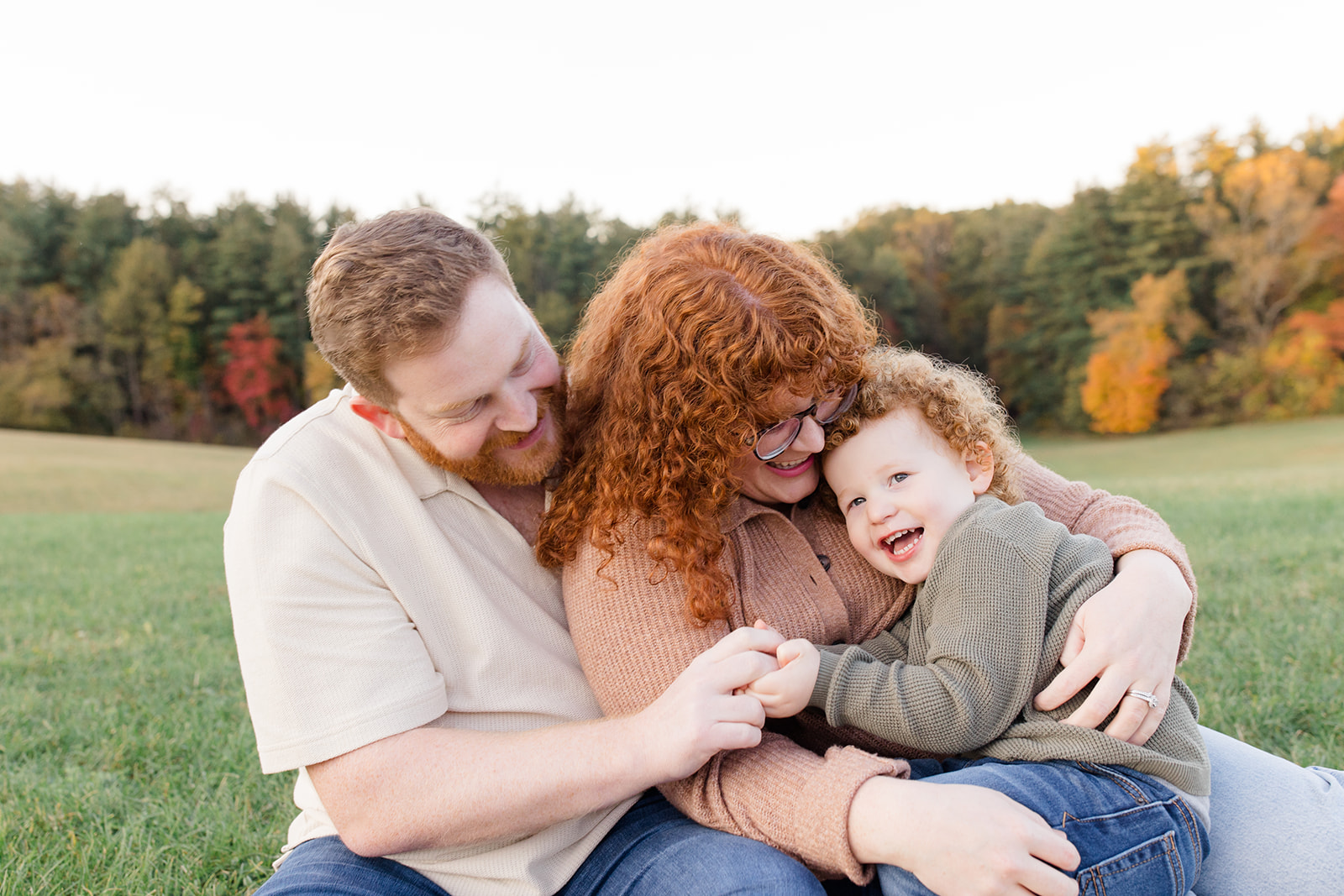 fall family photos with family og three sitting together on a blanket in a field at golden hour snuggling together and laughing captured by Cleveland family photographer