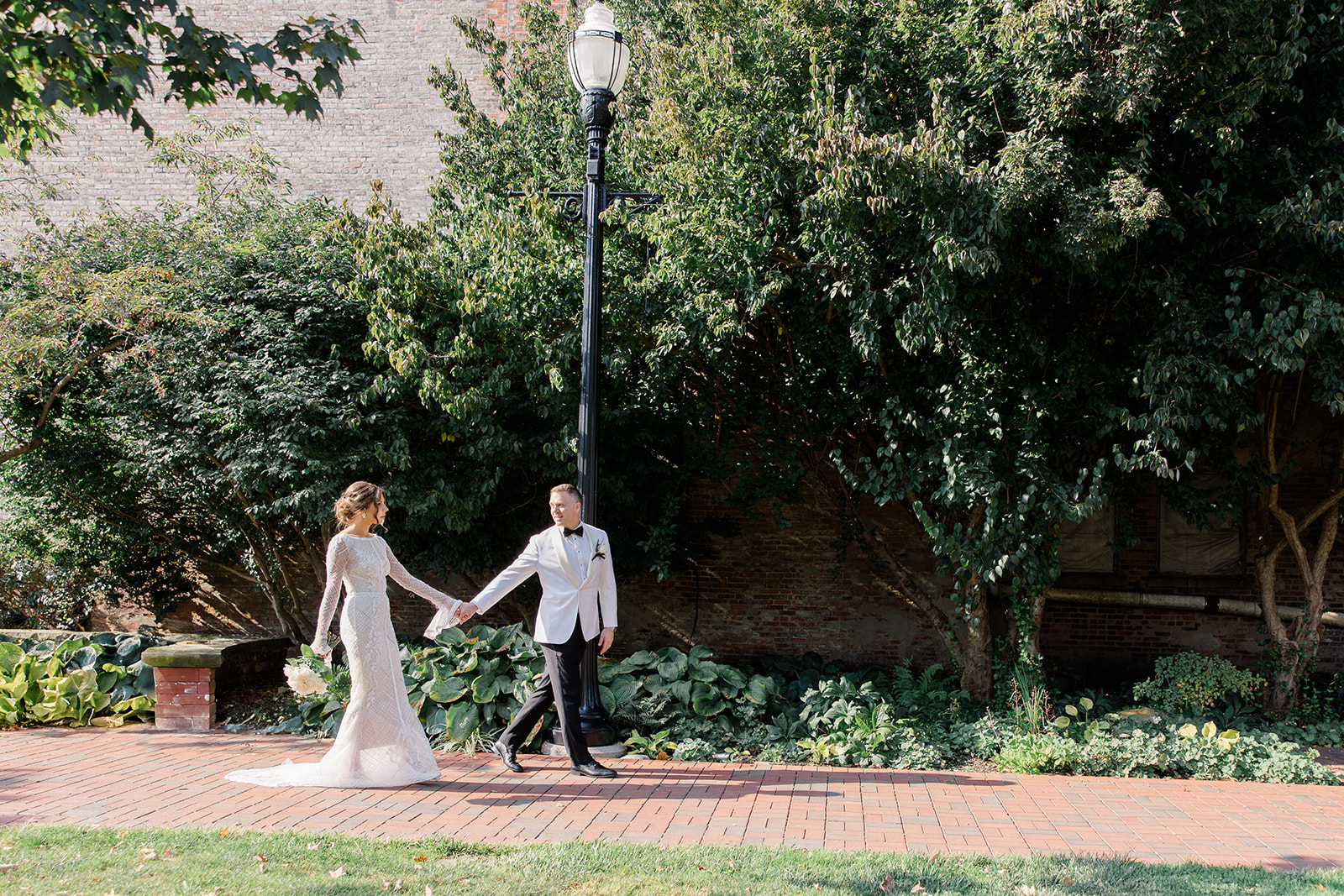 Bride and groom holding hands while walking along a brick path outside a garden near a Cleveland wedding chapel, captured by a Cleveland wedding photographer.