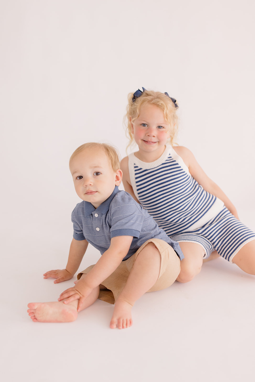 Brother and sister sitting together on the floor in a photo studio during a sibling portrait, photographed by a Cleveland family photographer.