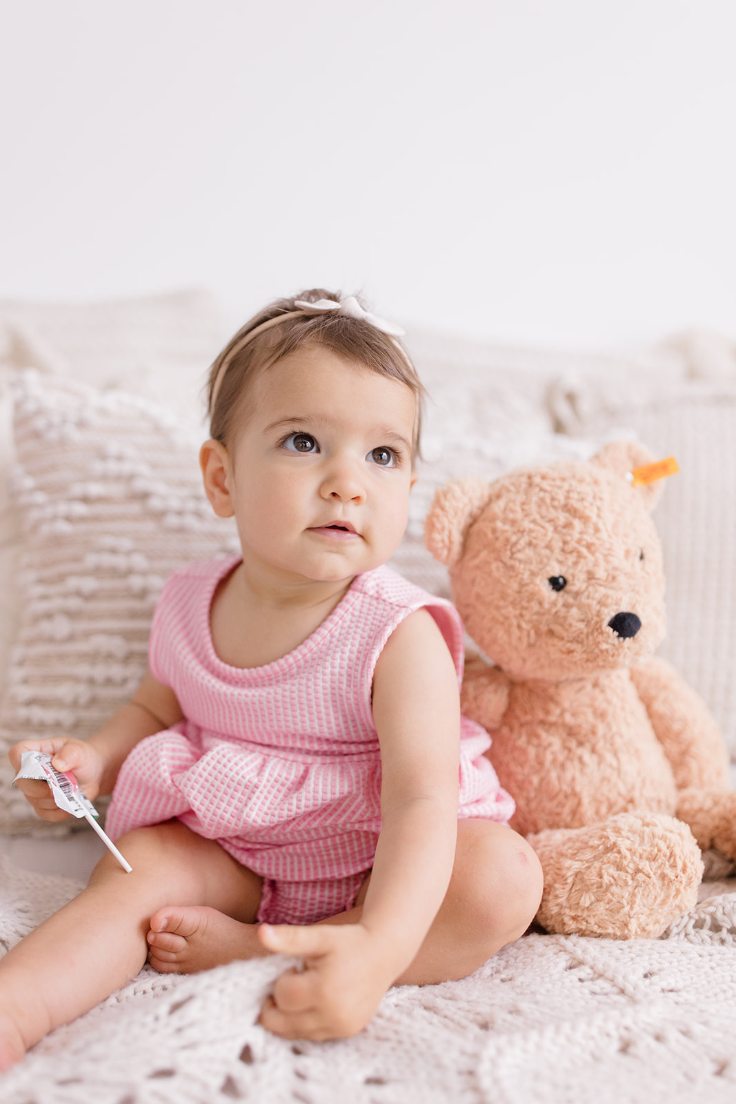 Baby in a pink dress sitting beside a teddy bear on a bed, Personality Portraits by a Cleveland family photographer.
